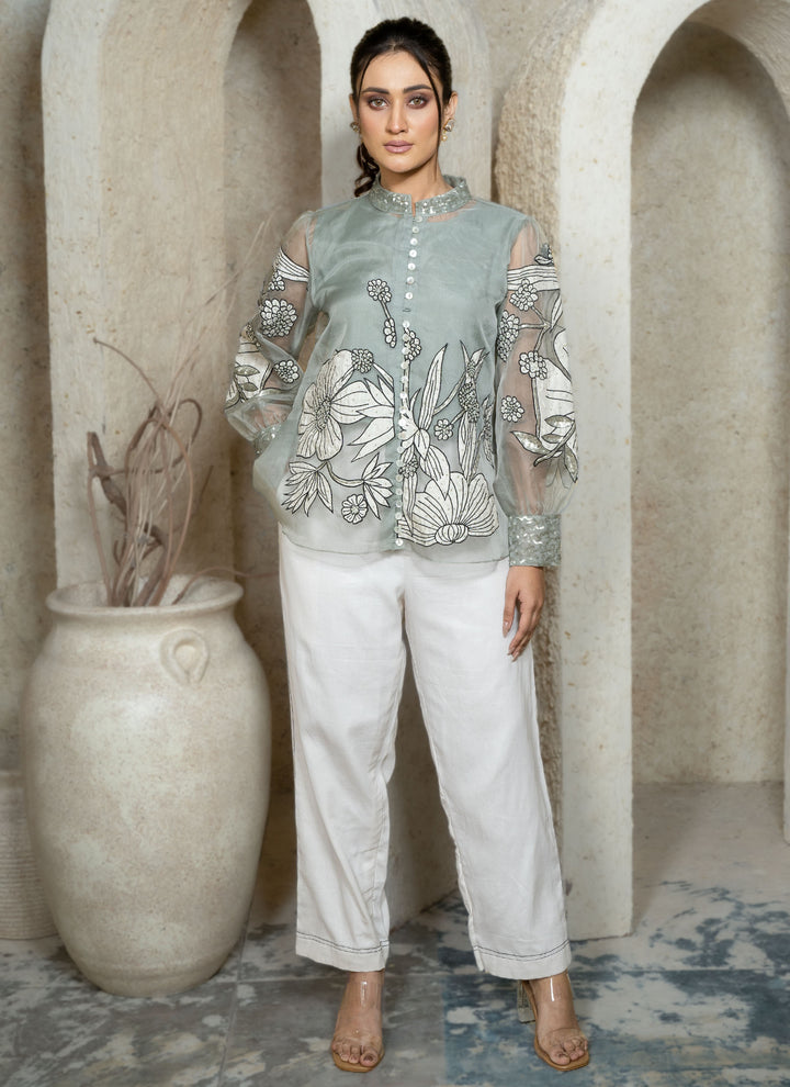 Woman wearing a dusty blue embroidered coord set with floral patterns along with white pants