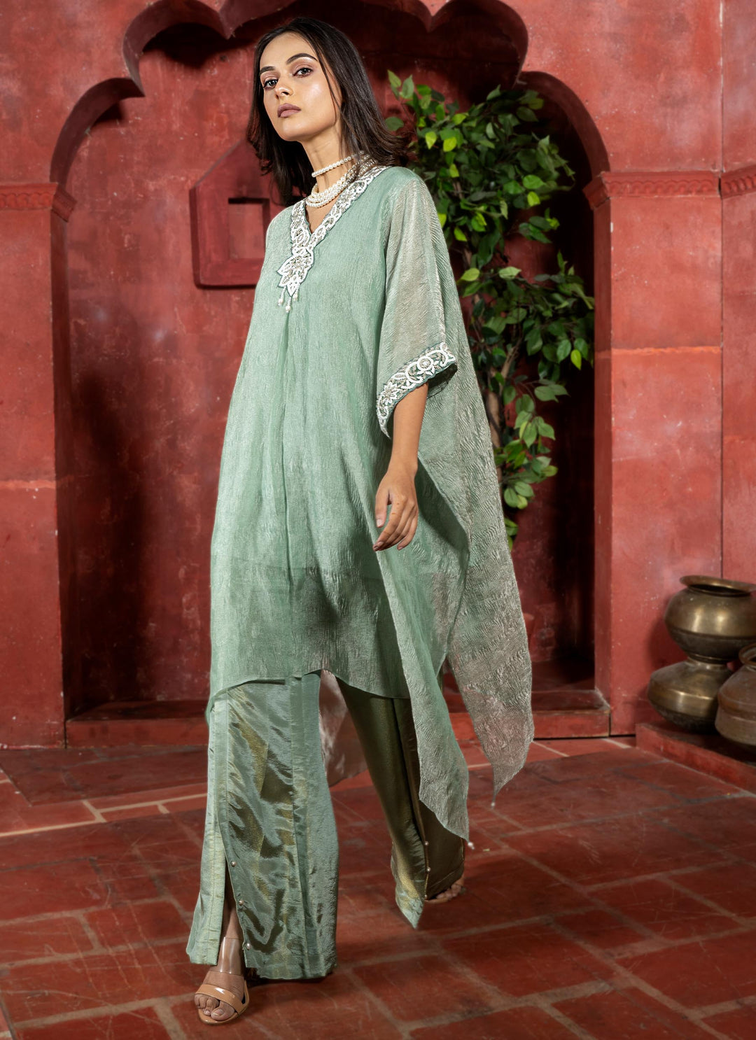 Woman in a green traditional outfit standing in front of a red archway with plants.
