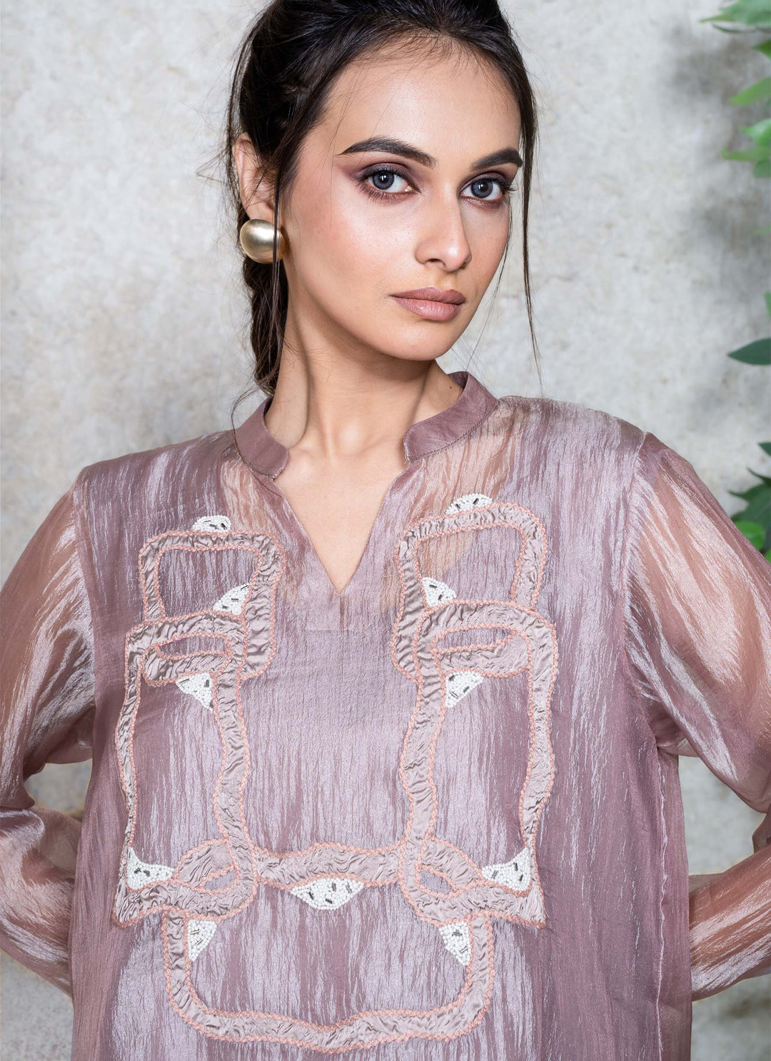 Woman wearing a light mauve embroidered top against a neutral background