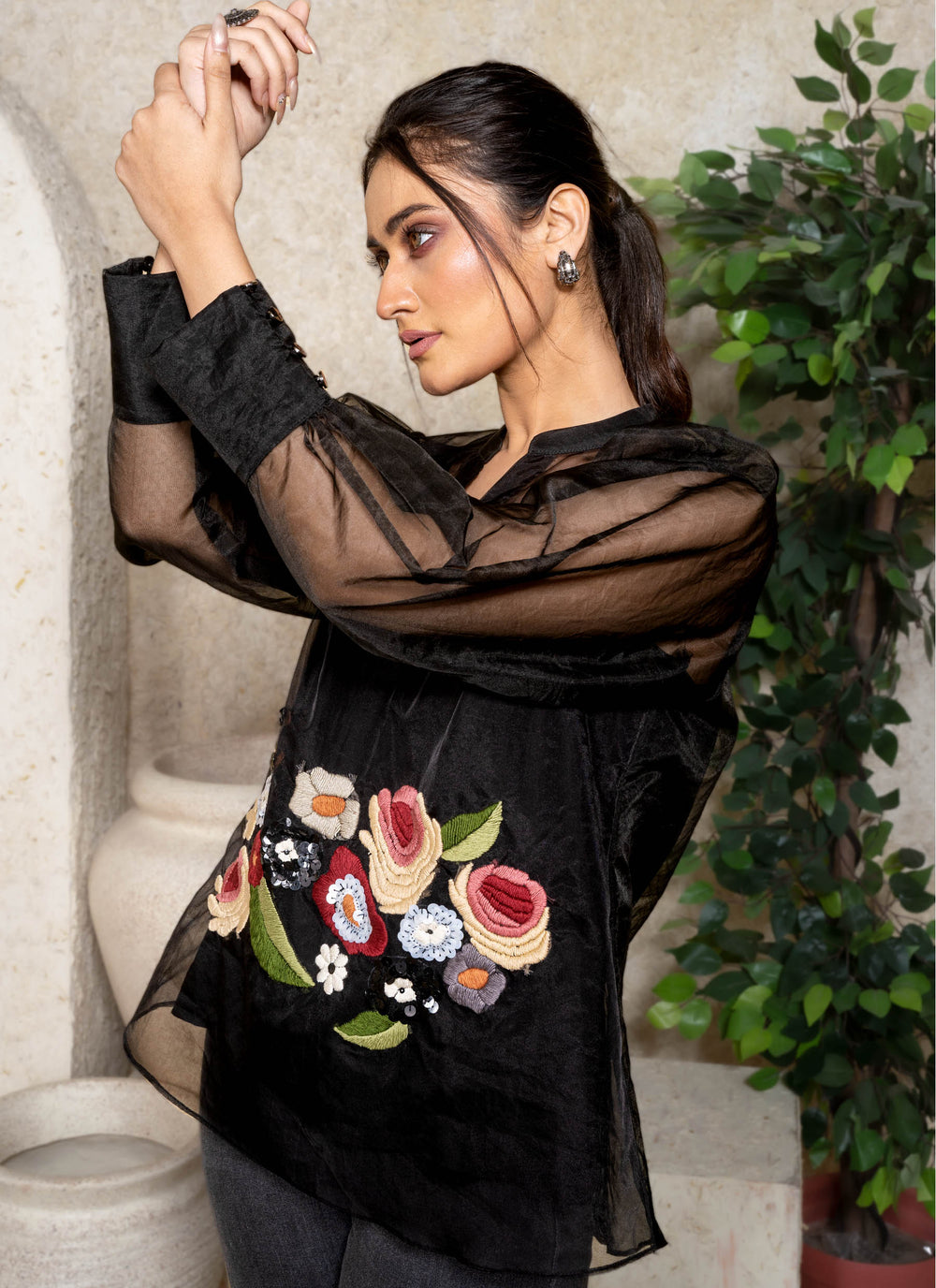 Woman wearing a black sheer top with floral embroidery in an indoor setting.