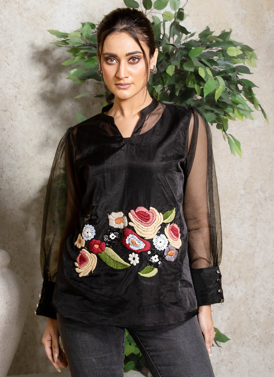 Woman wearing a black top with floral embroidery against a neutral background
