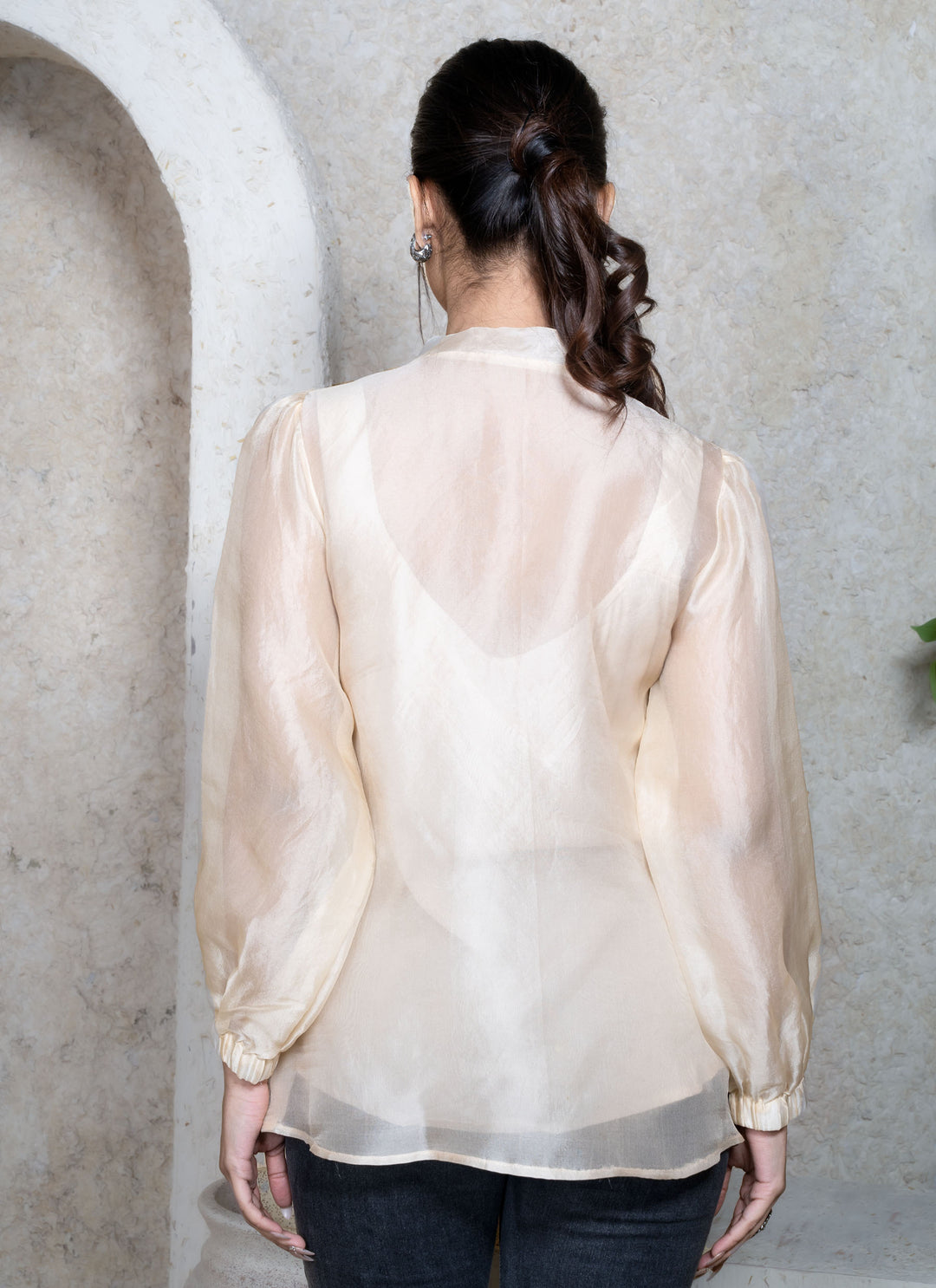 Woman wearing a cream sheer top against a natural background