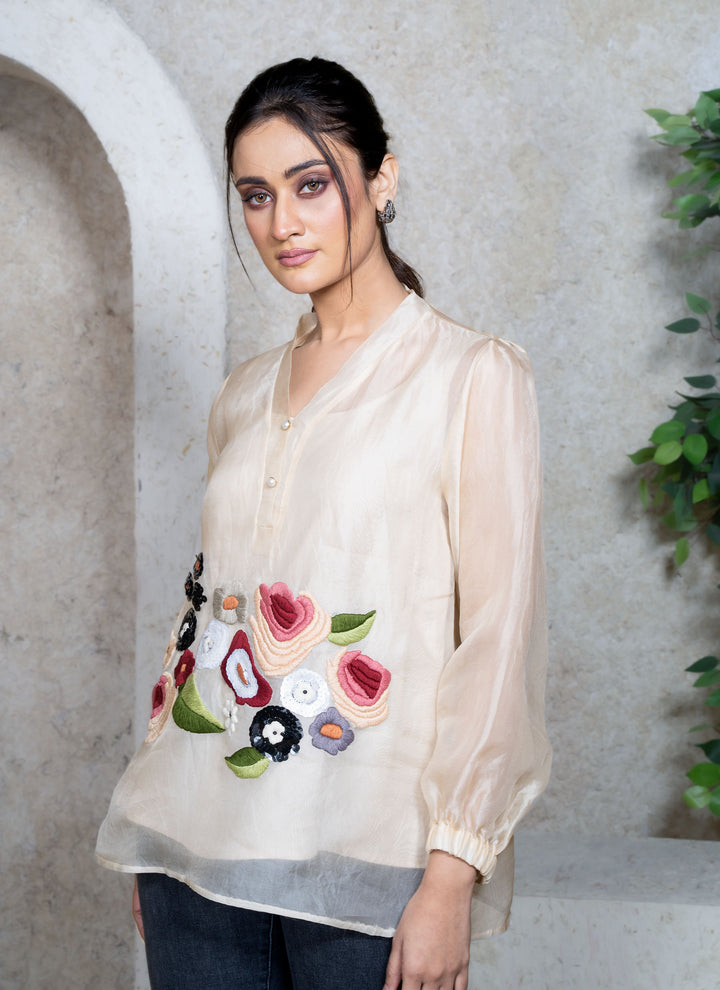 Woman wearing a cream top with floral embroidery standing in a natural setting.
