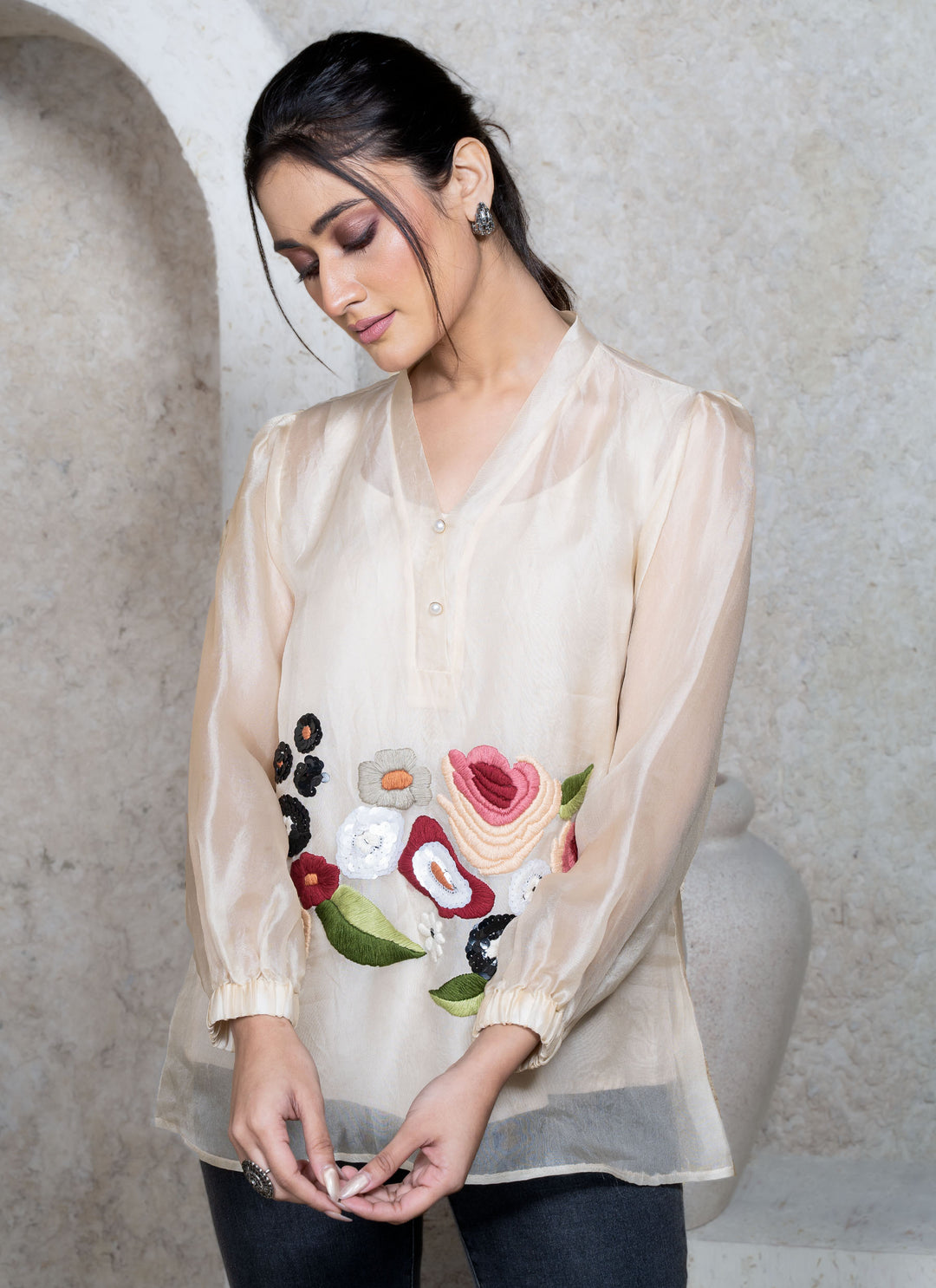 Woman wearing a cream top with floral embroidery against a neutral background