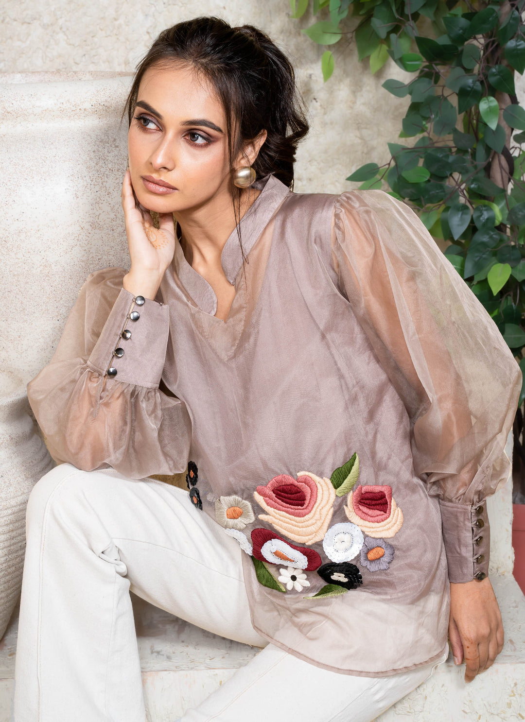 Woman wearing a champagne top with floral embroidery sitting outdoors.