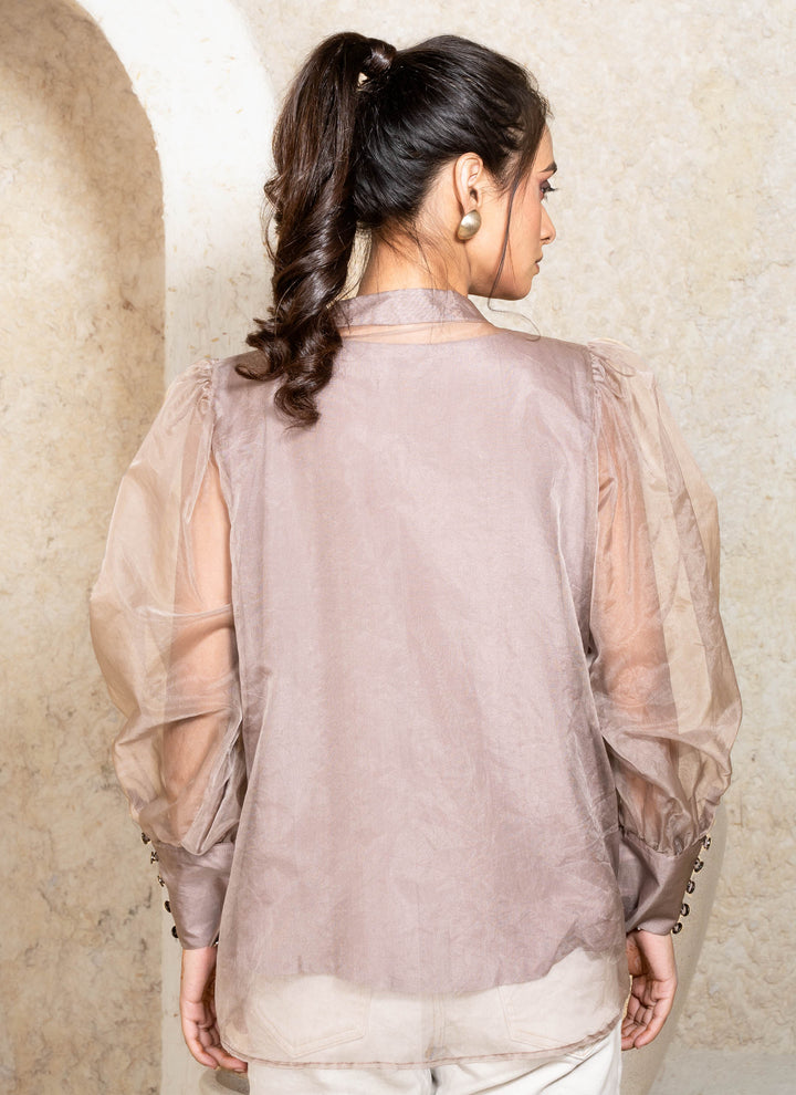 Woman wearing a sheer champagne top with her back against a neutral background
