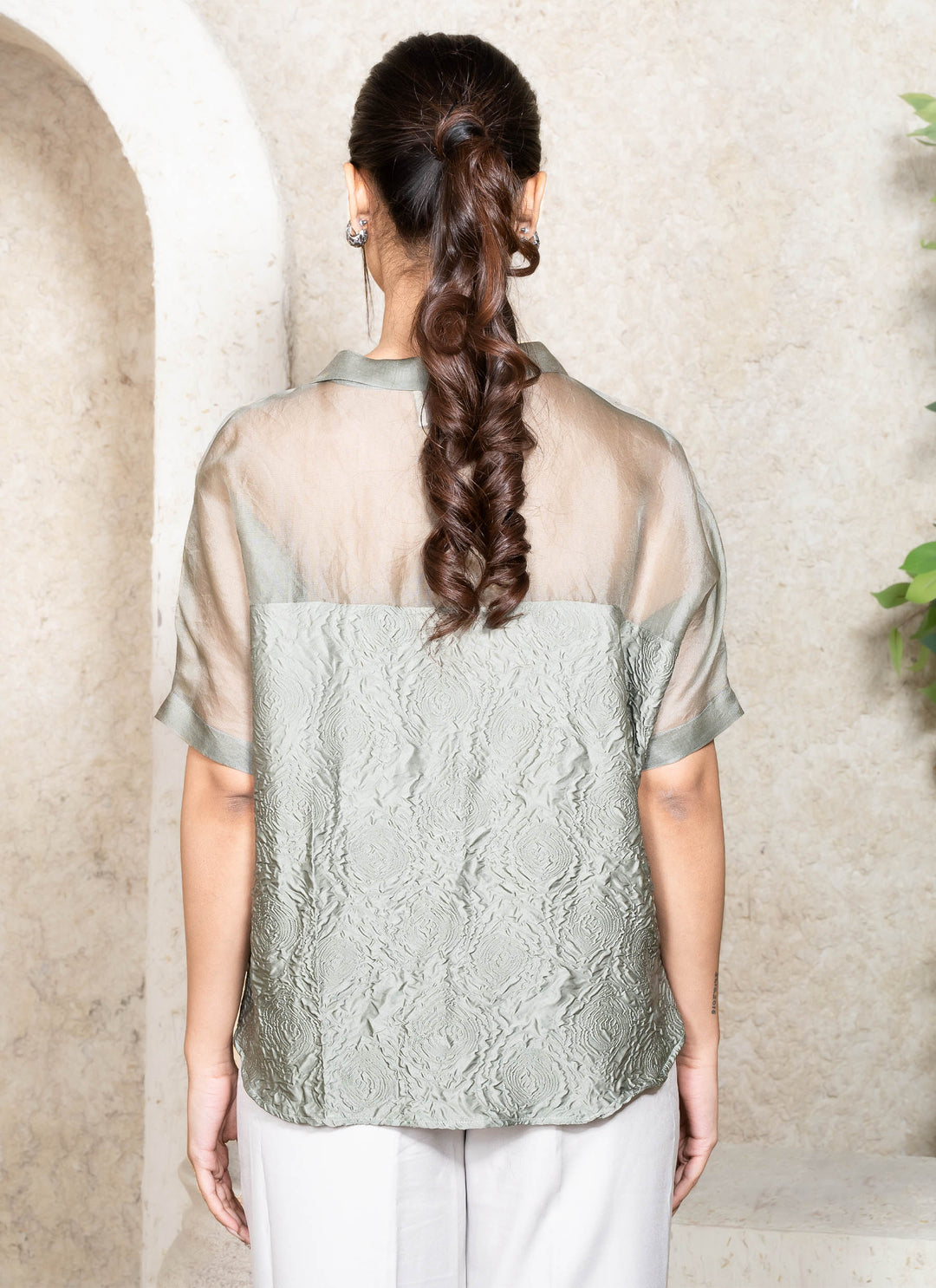 Woman wearing a green kaftan top with her back showing against a neutral background.