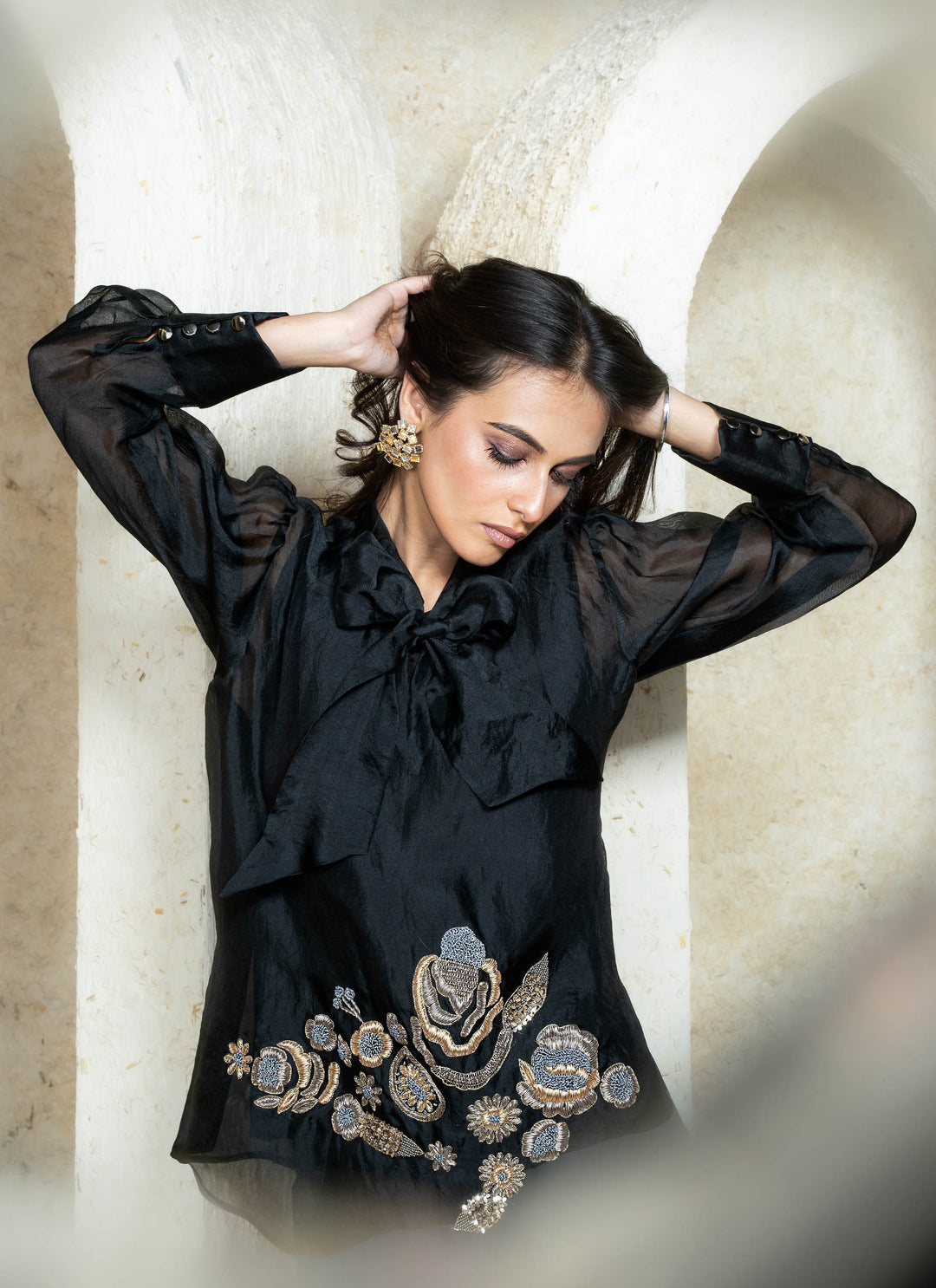 Woman wearing a black zardozi outfit with floral embroidery against a beige wall.