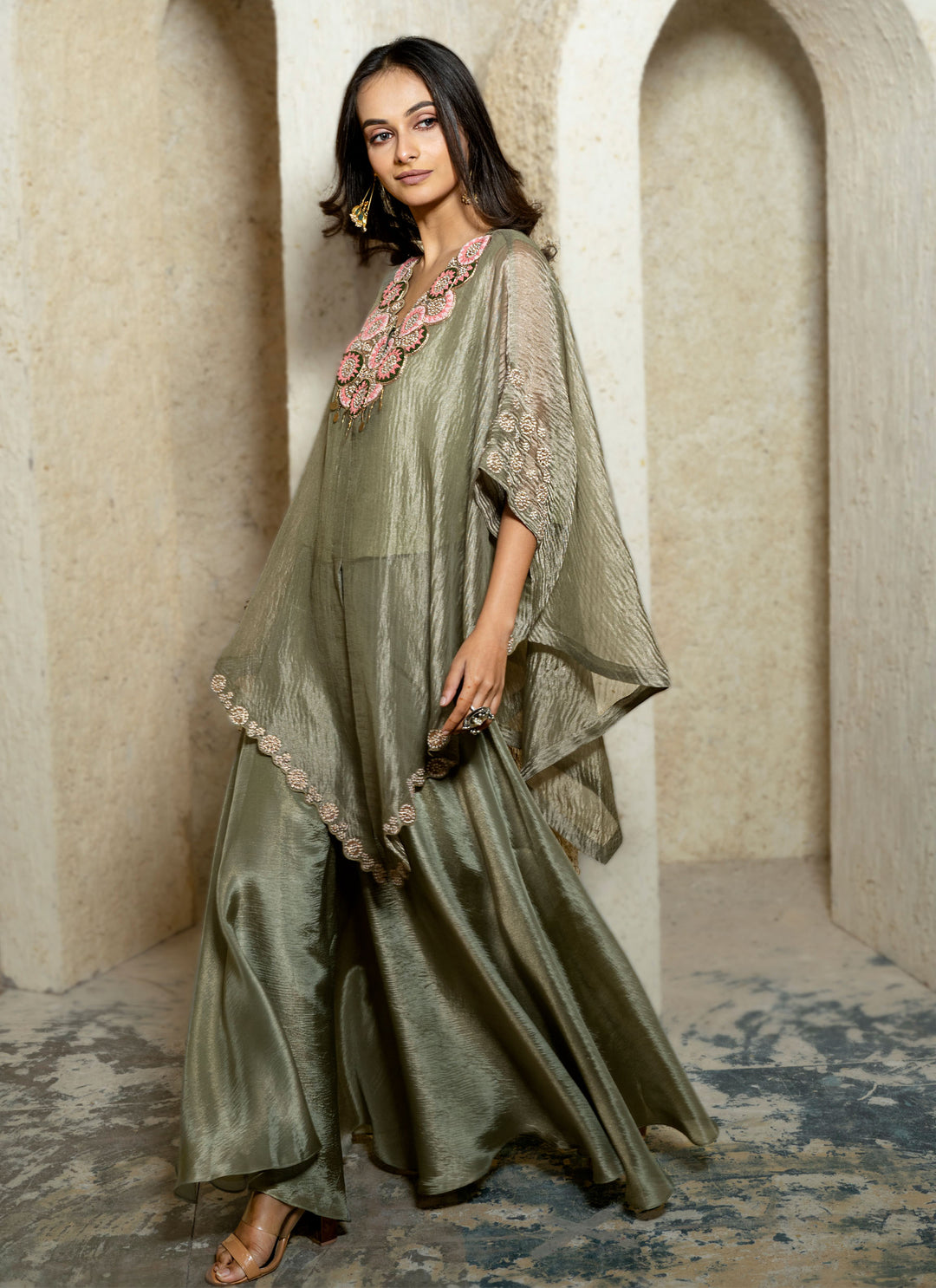 Woman wearing a green traditional kaftan outfit with floral details in an archway setting