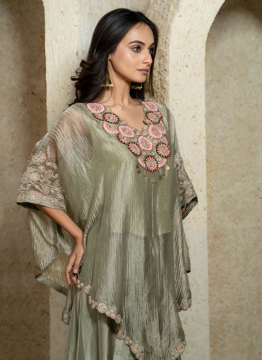 Woman wearing a light green embroidered kaftan against a beige wall.