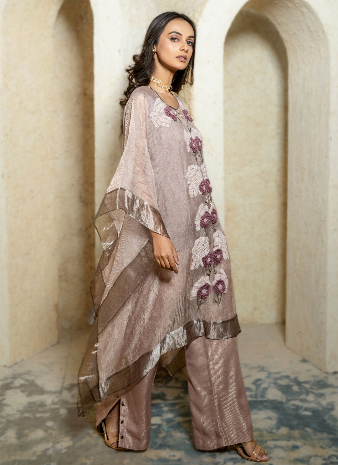 Woman in a pink floral hand embroidered kaftan outfit standing in an archway