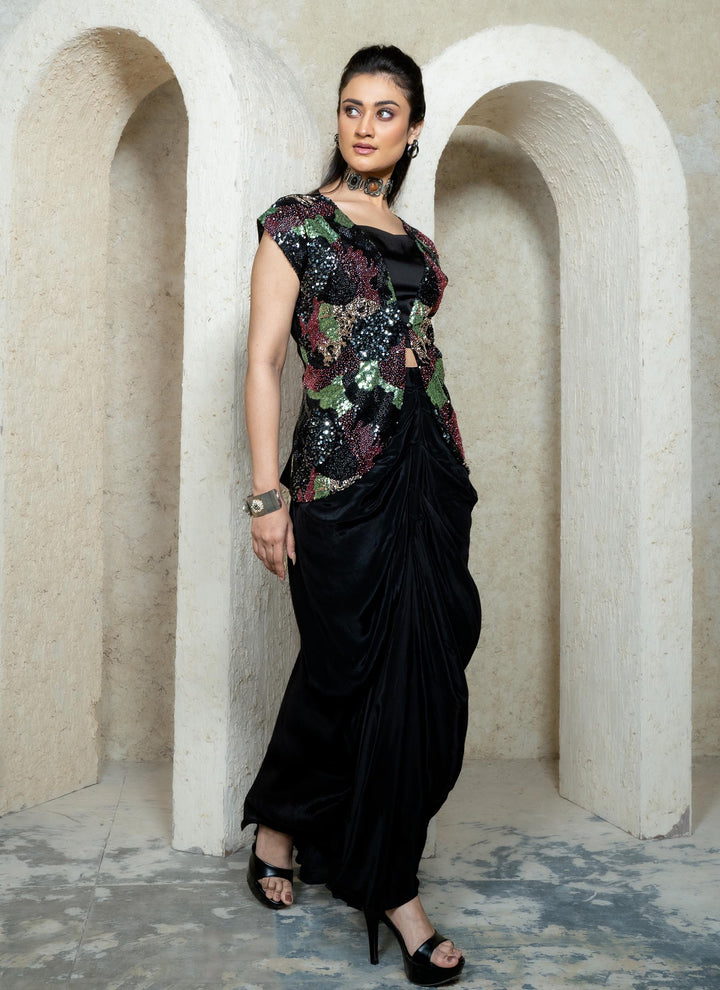 Woman in a black drape skirt with abstract sequins embroidered open jacket with bustier standing in an archway.