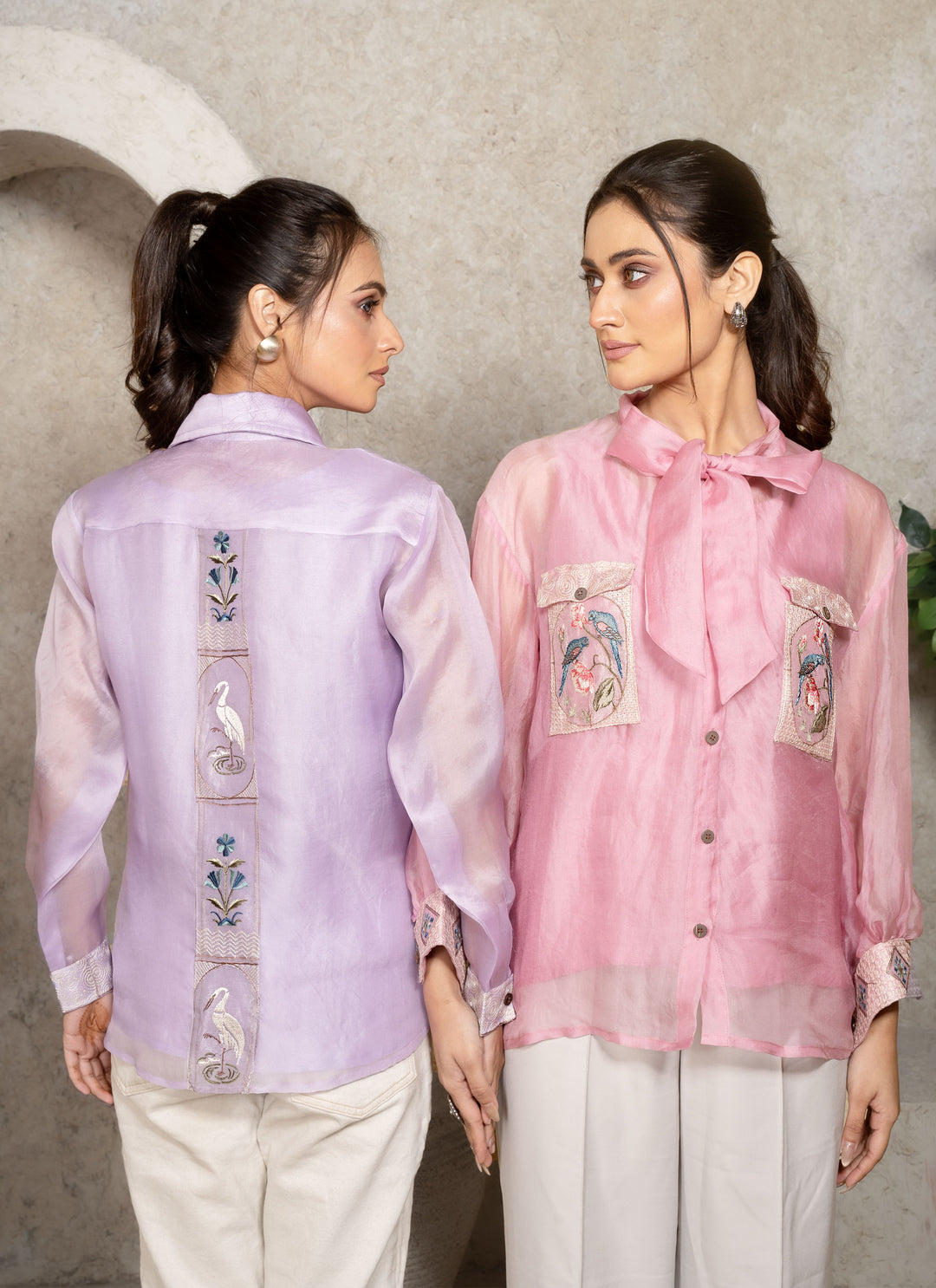 Two women wearing embroidered shirts against a neutral background