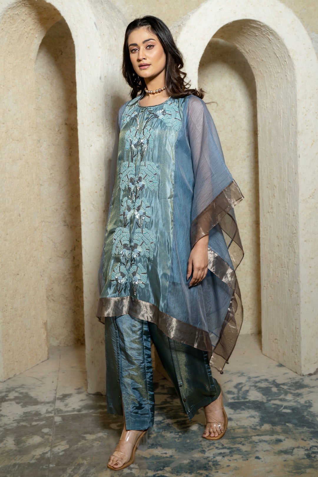 Woman wearing a blue embroidered kaftan set walking in front of a beige background
