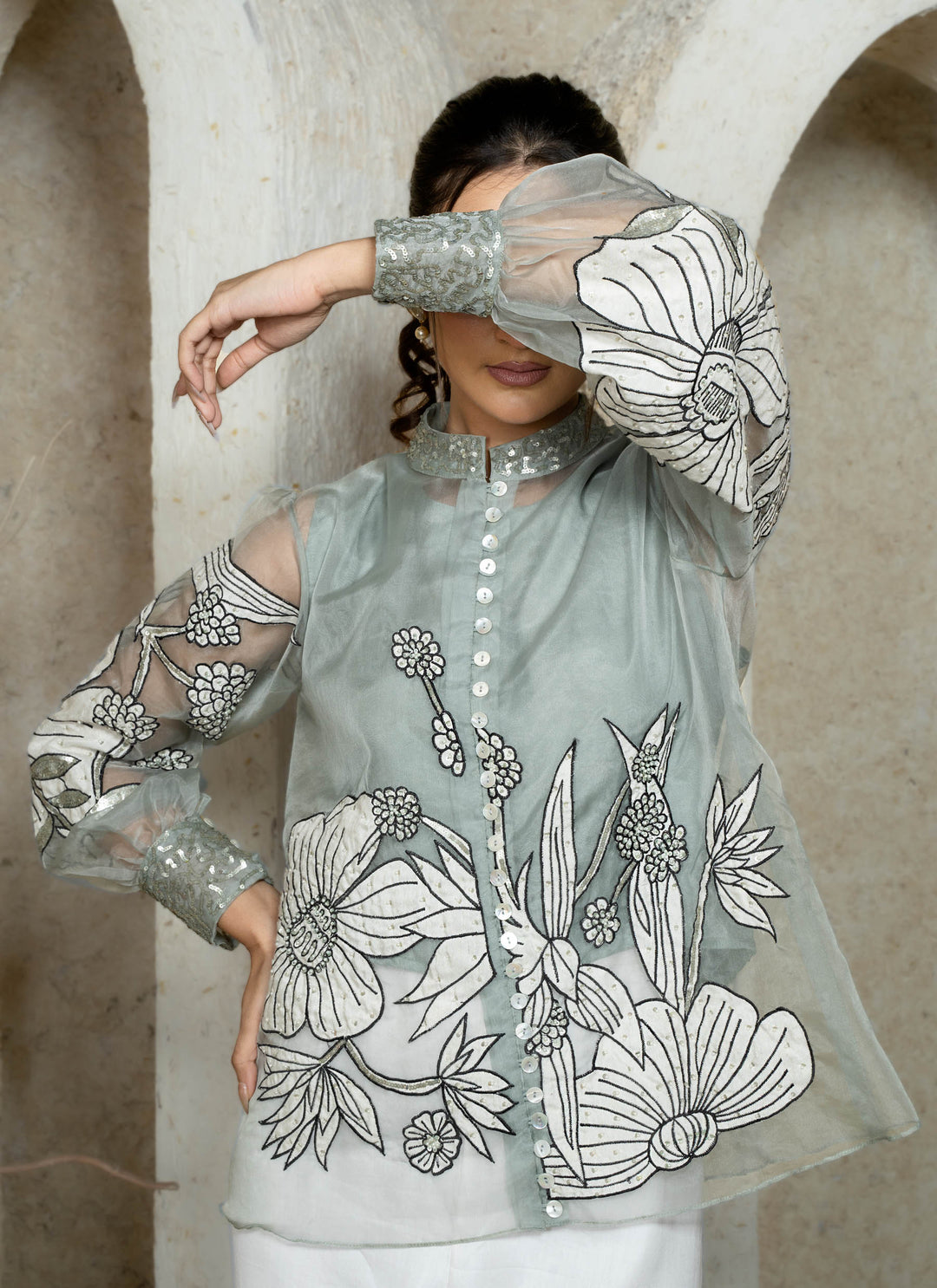 Woman wearing a dusty blue embroidered coord set with floral patterns along with white pants against a white background