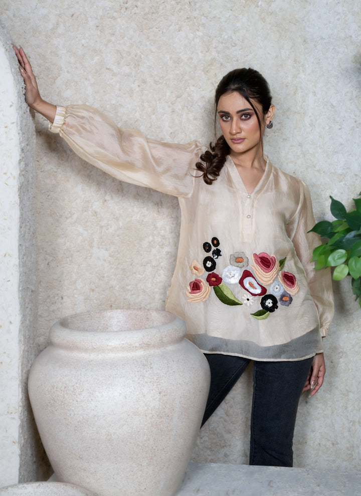 Woman wearing a beige top with floral embroidery walking against a natural background.